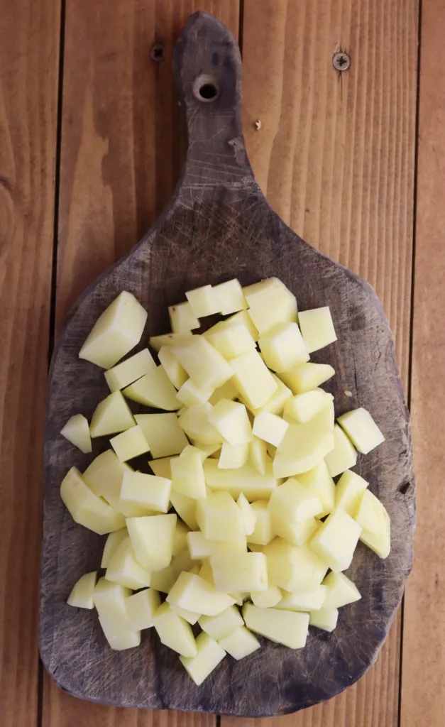 pealing the potatoes and cutting them into small pieces before adding them to a pot with other ingredients