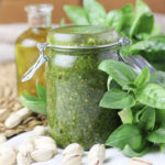 image of basil pesto with pistachios in a jar, with pistachios and olive oil in the background