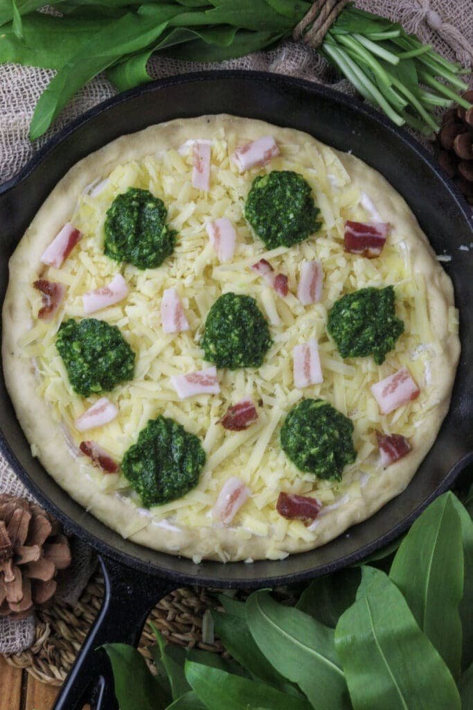 image of pizza dough topped with wild garlic pesto and smoked bacon slices