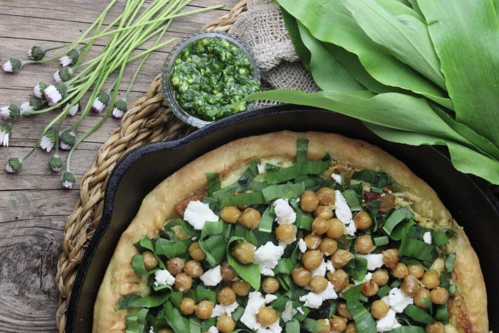 image of wild garlic pizza in a pan with roasted chickpeas and wild garlic leaves in the background
