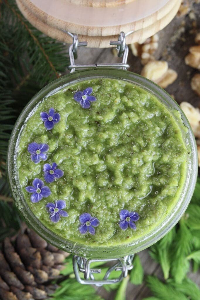 Image of spruce tip pesto in a jar with wild flowers