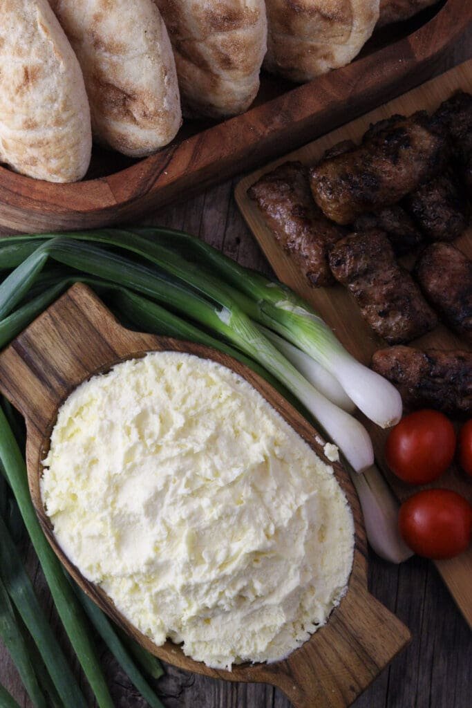 A bowl of kajmak served with cevapi, lepinje, young onions and tomatoes.
