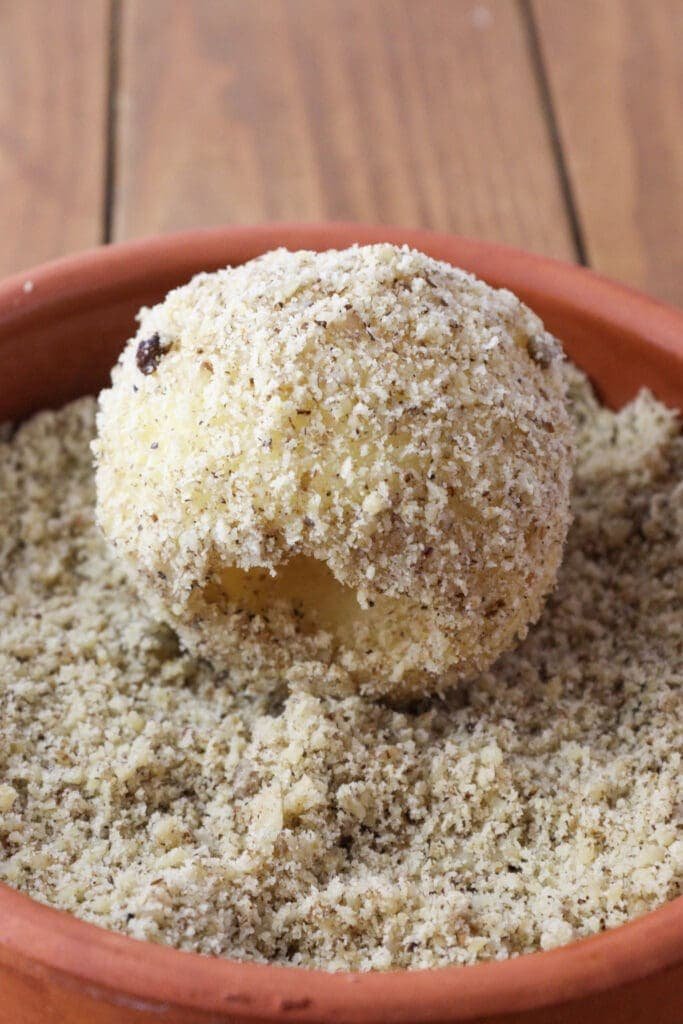 Cooked apple being rolled in ground walnuts