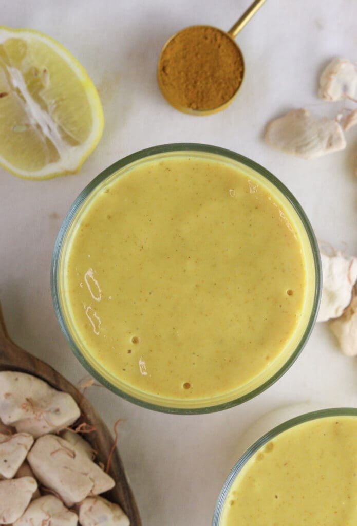 Image of a glass of baobab ginger smoothie from above, with baobab fruit pulp, turmeric and lemon in the background