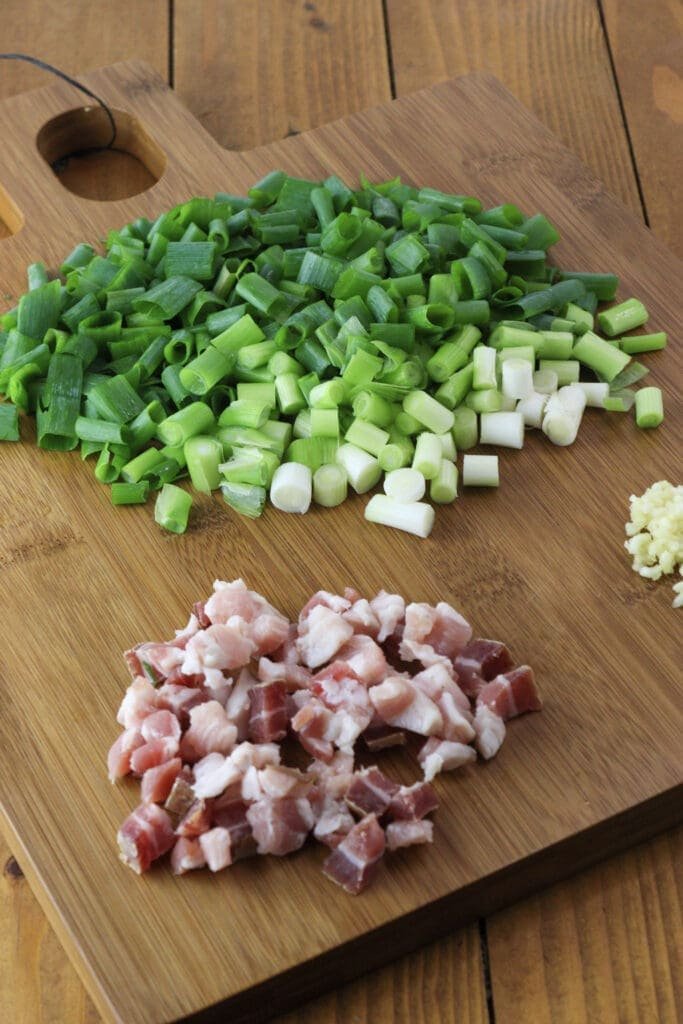 Chopped young onion, smoked bacon and garlic on a wooden cutting board