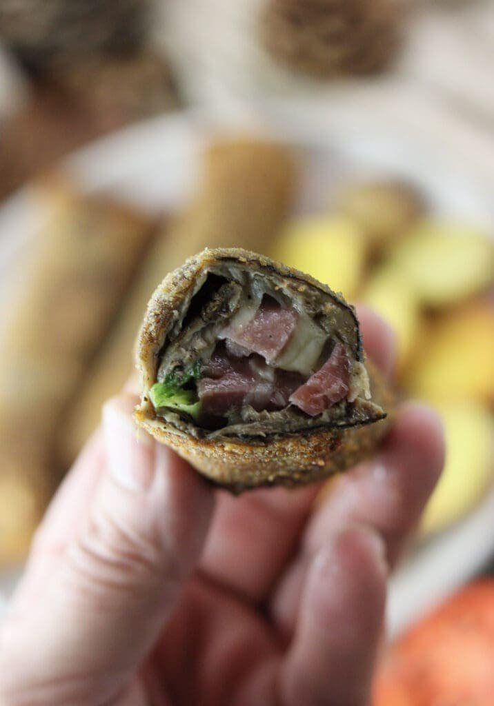 A close shot of sliced fried parasol mushroom roll held in hand, with melted mozzarella, bacon and fresh young onion slices inside the roll.