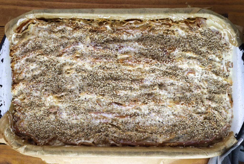 Baking the pie by chicken of the woods pie recipe - topping the phyllo sheets with sour cream and eggs, and sesame seeds on top.