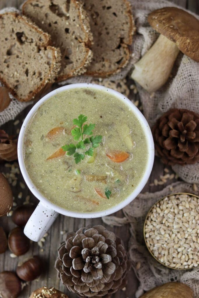 A bowl of mushroom soup with porcini mushrooms, bread and chestnuts in the background