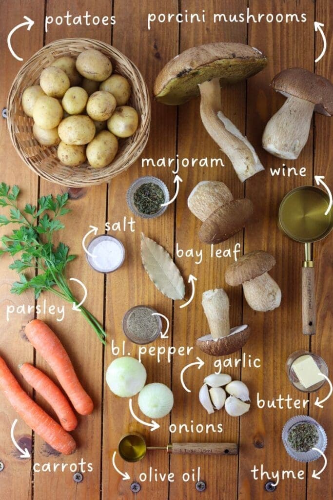 a top shot of igredients needed for porcini soup: porcini mushrooms, potatoes, carrots, onions, garlic, white wine, bay leaf, olive oil, salt, pepper, butter, thyme and marjoram