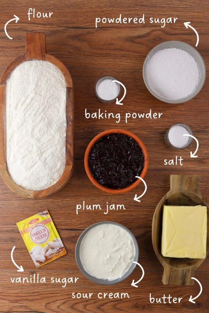 gathering ingredients for empanada cookies: flour, butter, sour cream, salt, baking powder, powdered sugar, vanilla suga and plum jam