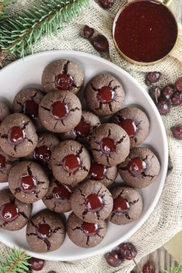 A plate of buckwheat cookies with strawberry jam with rose hip buds, spruce branch and cup of jam.