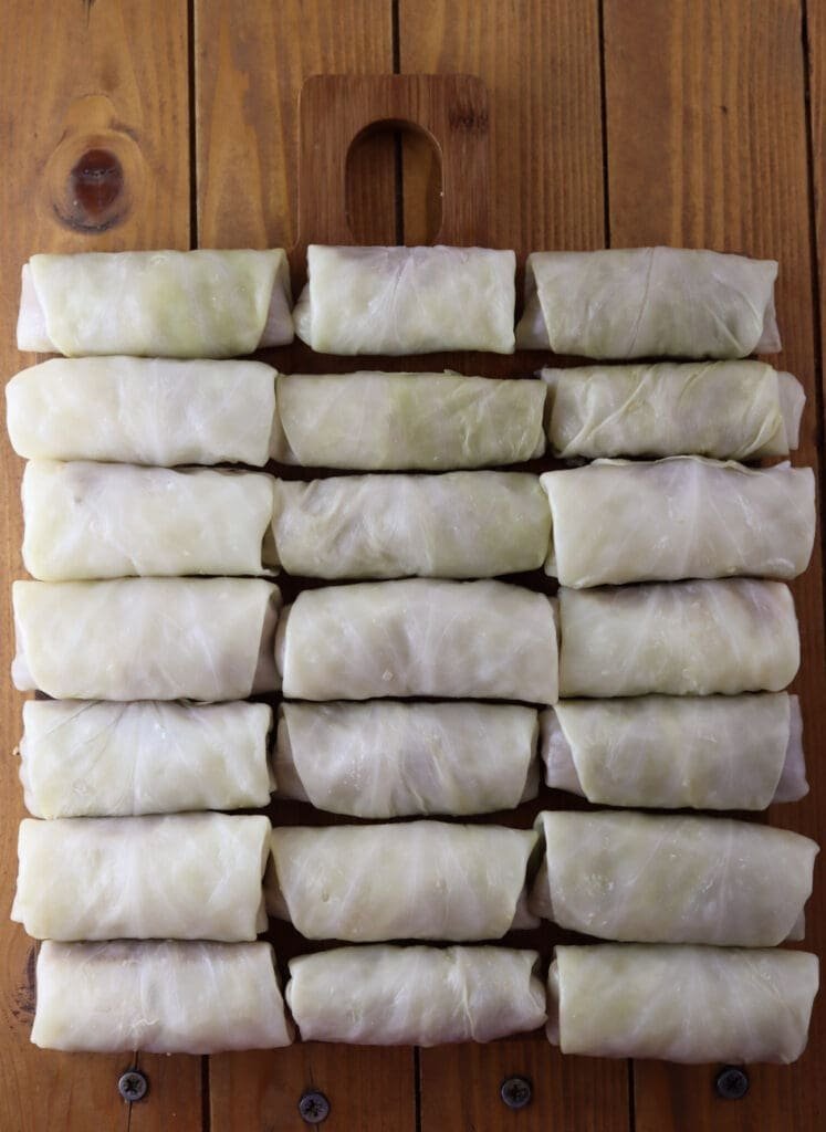 21 buckwheat stuffed cabbage rolls on a wooden cutting board waiting to be added to a baking pot before cooking in the oven.