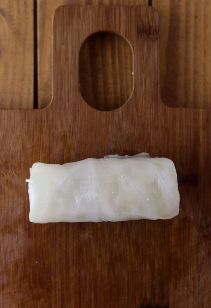 A decently rolled stuffed cabbage roll on a wooden cutting board.