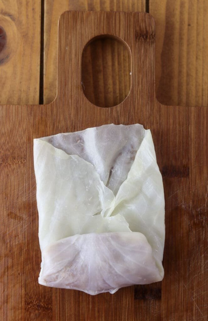 How to roll the cabbage leaf stuffed with the filling - tucking the edges and rolling towards the leaf's outside.