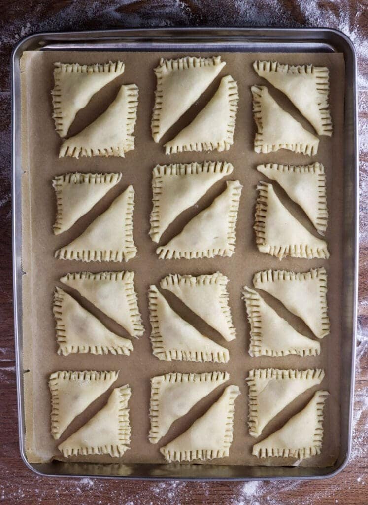 Cookies filled with craclings are placed on parchment paper on a baking tray.