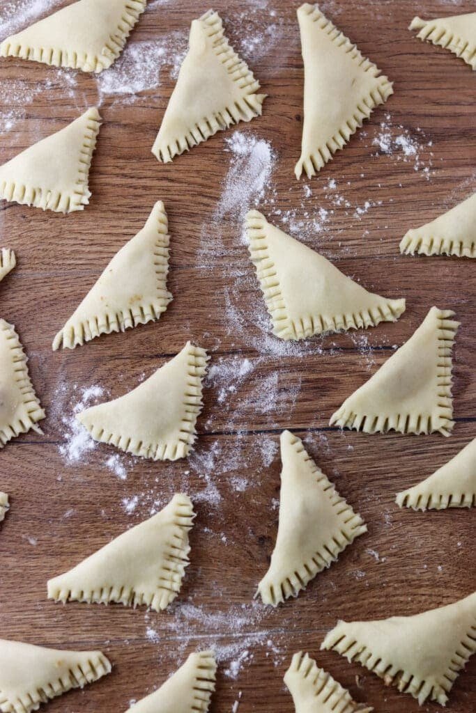 Making little pocket cookies that are filled with pork craclings, the edges are pressed down with a fork.