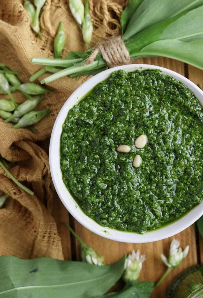 Pesto with wild garlic, olive oil and toasted pine nuts with wild garlic buds and flowers in the background.