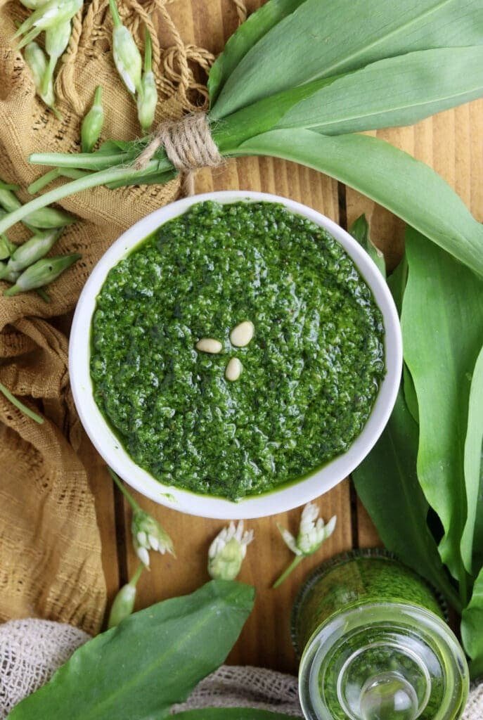 Another bowl of dark green wild garlic pesto, ready to be served with pasta. There are some wild garlic flower buds in the background.