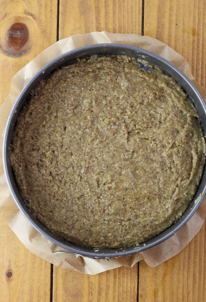 Adding the cake batter on the plum halves in a round cake baking pan.