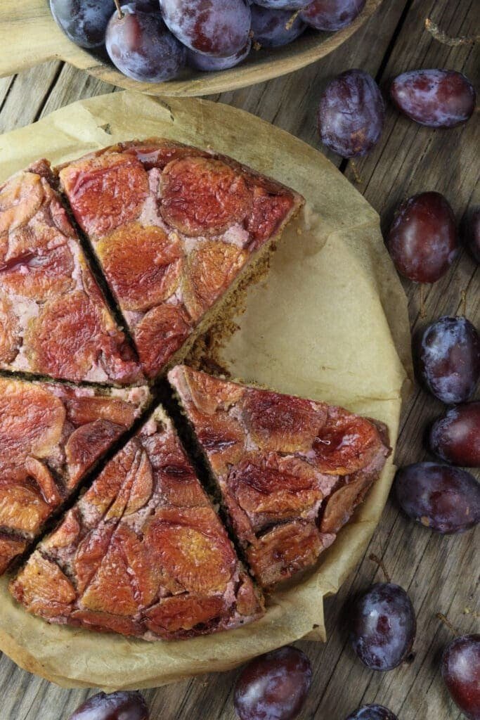 Sliced buckwheat upside down cake with fresh plums in the background.