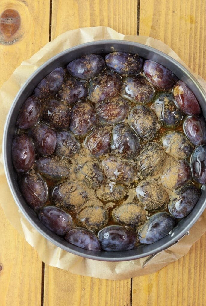 pouring honey and sifting cinnamon over the plums before adding the cake batter into a cake baking pan