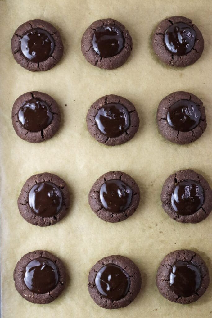 Buckwheat thumprint cookies filled with chocolate filling resting on a baking sheet.