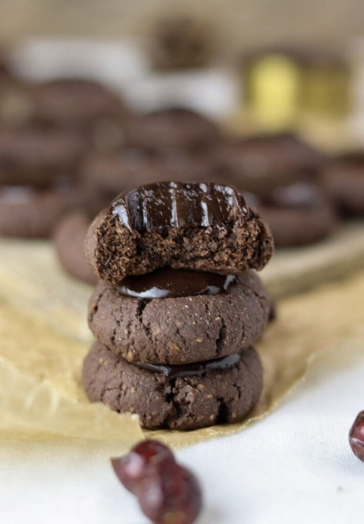 Three buckwheat thumbprint cookies stacked, the top cookie has been biten in half and showing a delicious chocolate filling in the center.
