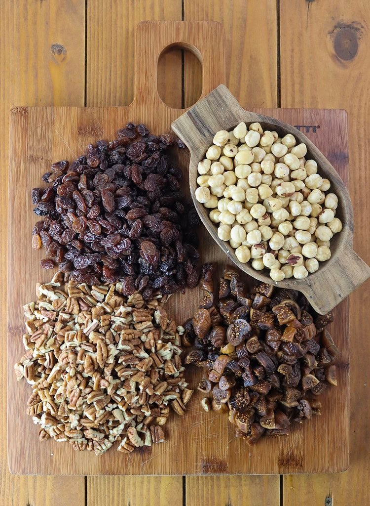 Chopped hazelnuts, pecans, raisins and dried figs on a wooden cutting board.