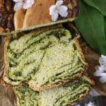 Slices of wild garlic bread with wild garlic leaves and cherry flowers in the background.