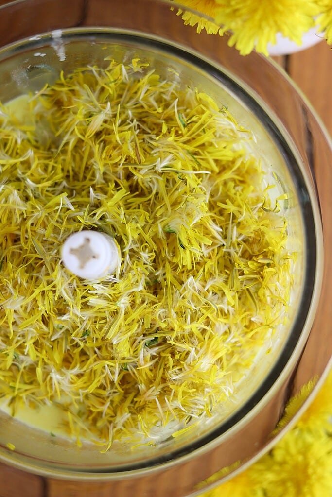 How to add dandelion flower petals to the heavy cream mixture in a blender, with dandelion flowers in the background.