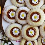 Dandelion thumbprint cookies with flowers on a white plate with dandelion petals in the background.