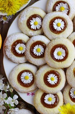 Dandelion thumbprint cookies with flowers on a white plate with dandelion petals in the background.