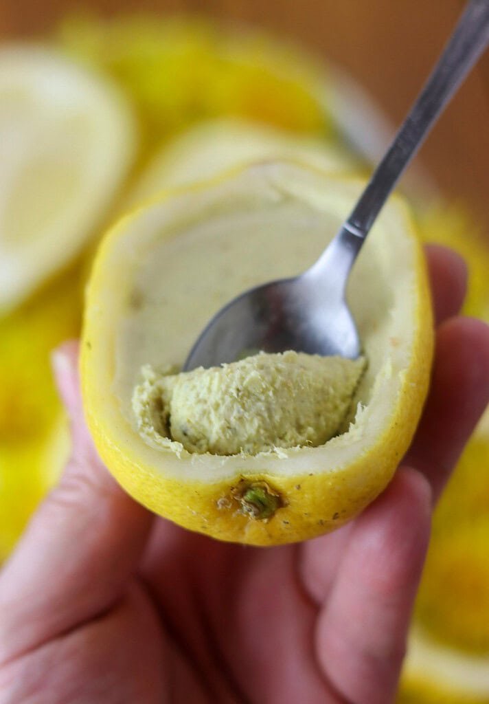 Holding a lemon shell in hands, with a dandelion dessert inside and a small teaspoon in the shell.