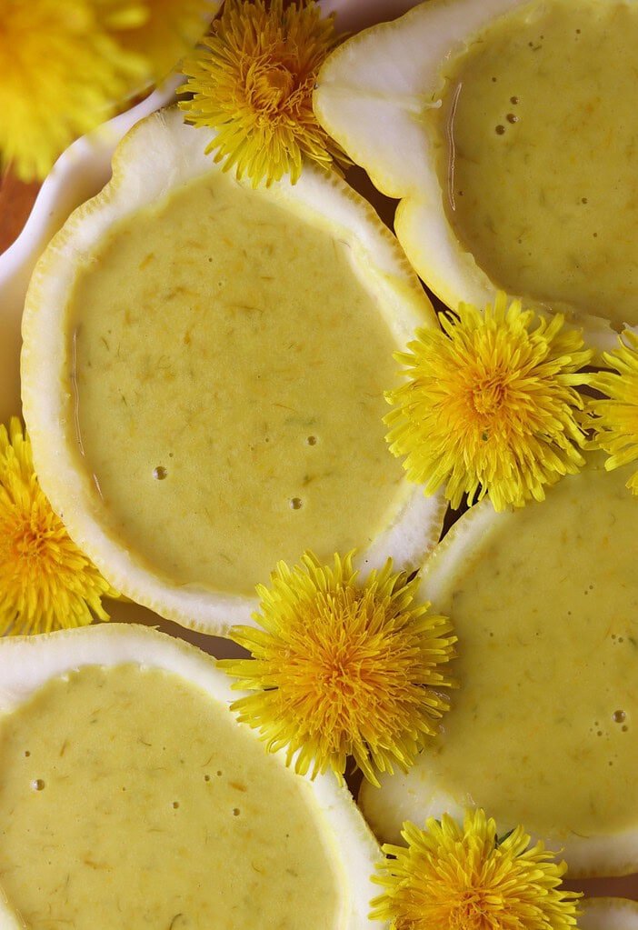 Dandelion dessert in lemon shells on a wooden board, surrounded by fresh dandelion flowers.