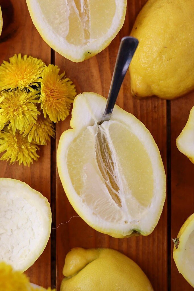 Hollowing out a lemon shell with a spoon to prepare it for dandelion dessert filling, on a wooden surface.